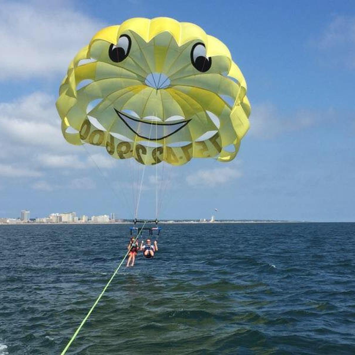 Two people enjoying a parasail flighting with a bright yellow smiley parasail