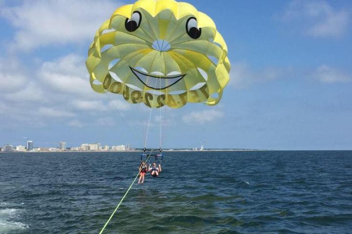 Two people enjoying a parasail flighting with a bright yellow smiley parasail