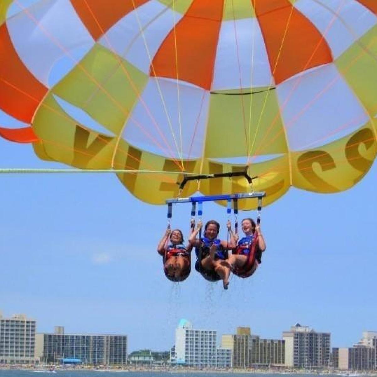 Three ladies parasailing in a bright green and orange parasail